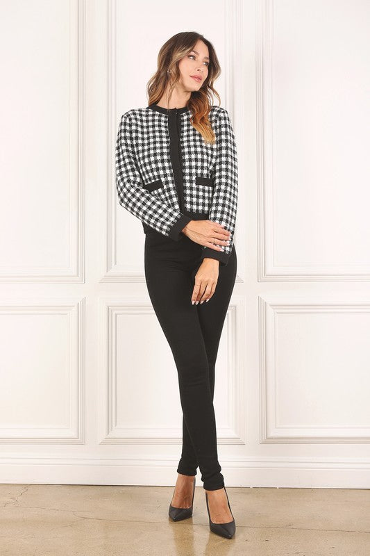 A woman dressed in the Black Check Knitted Jacket, featuring snap buttons and functional pockets, complemented by black pants, stands against a white background.