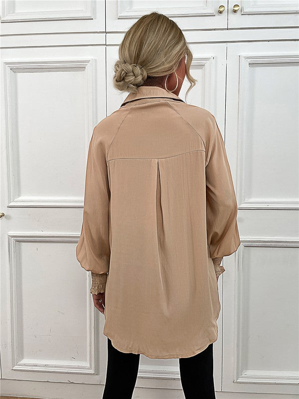 A woman wearing a Women's Long Sleeve Button Down Bluse with long puffy sleeves, made from 100% polyester, and layered necklaces stands in front of a white paneled wall.