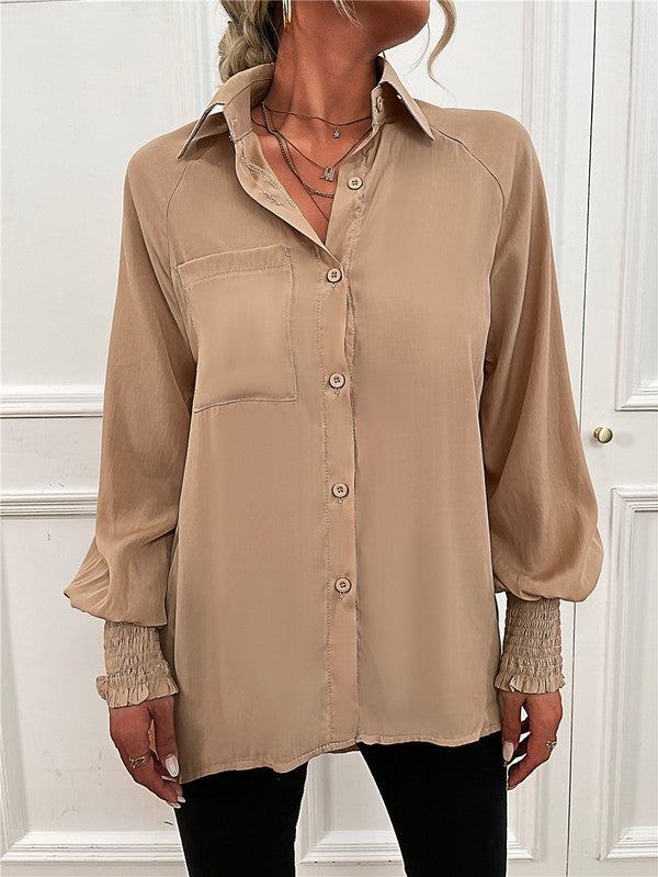 A woman wearing a Women's Long Sleeve Button Down Bluse with long puffy sleeves, made from 100% polyester, and layered necklaces stands in front of a white paneled wall.