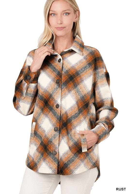 A woman is wearing a Yarn Dyed Plaid Shacket With Pockets in a rust color. One hand is on her collar while the other rests in her pocket. She has light hair and is looking forward.