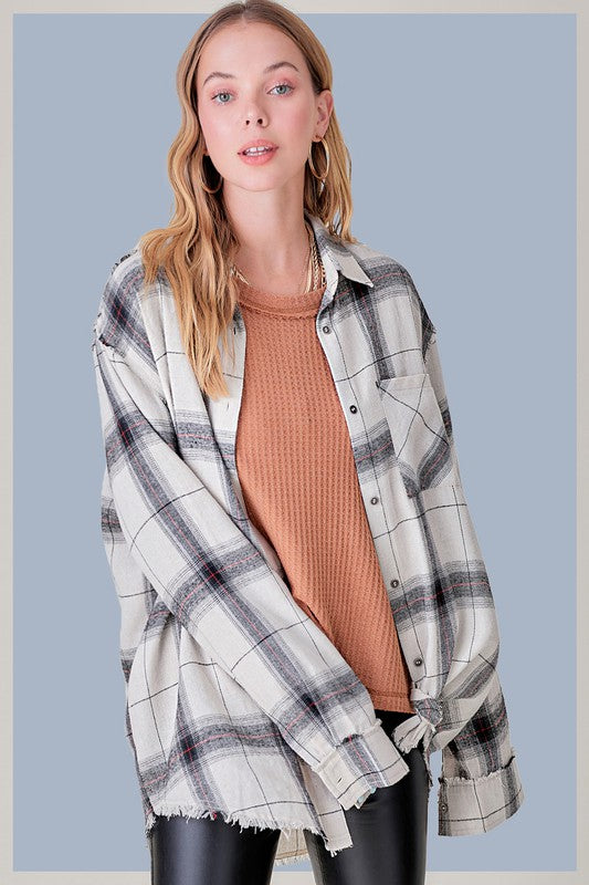 A person with long blonde hair wearing a black cap and an oversized Celine Shirt, which features a blue checkered plaid flannel design, showing a slight smile against a neutral background.