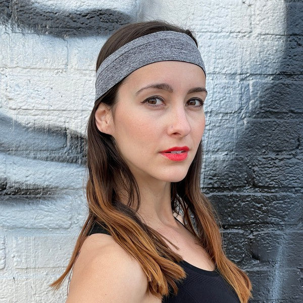 Woman with a pink Cardio Cross-Training Headband made of high-performance elastic fabric, standing against a black brick wall.