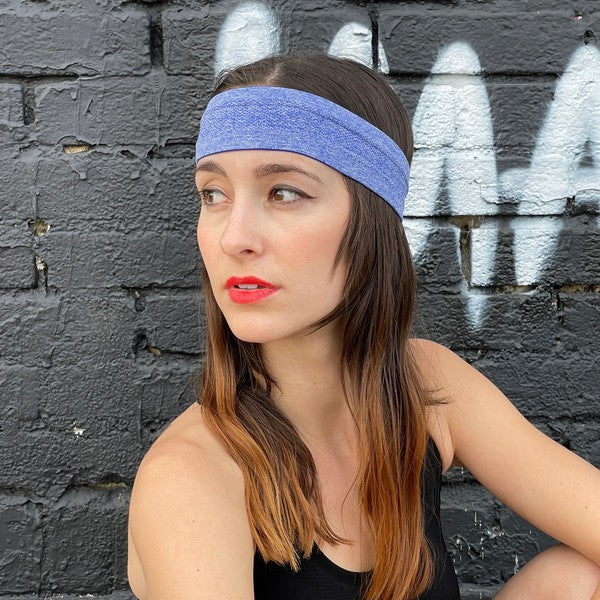 Woman with a pink Cardio Cross-Training Headband made of high-performance elastic fabric, standing against a black brick wall.