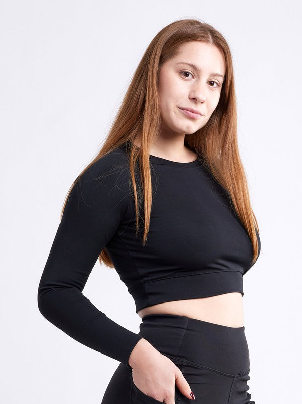 A person with long hair wears a seamless style, long-sleeve crop top and high-waisted bottoms; they stand with one hand on their hip against a plain white background.