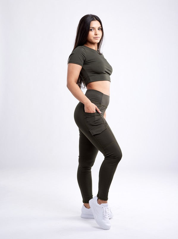 A person with long dark hair wears a fitted, olive green Short-Sleeve Crop Top and matching high-waisted leggings made from breathable material, standing against a plain white background.