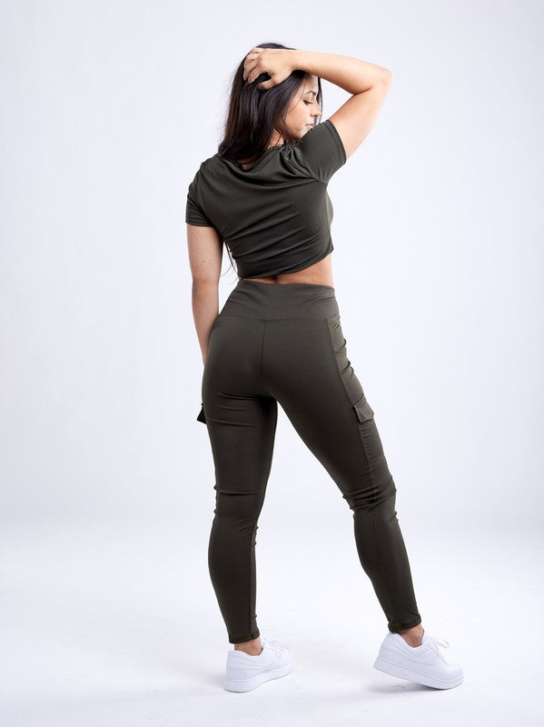 A person with long dark hair wears a fitted, olive green Short-Sleeve Crop Top and matching high-waisted leggings made from breathable material, standing against a plain white background.