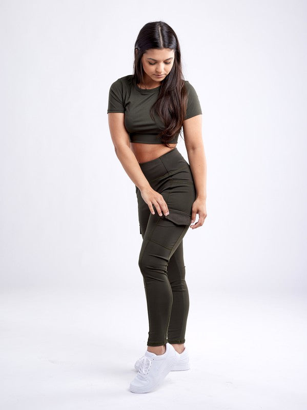 A person with long dark hair wears a fitted, olive green Short-Sleeve Crop Top and matching high-waisted leggings made from breathable material, standing against a plain white background.