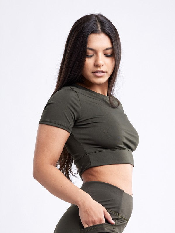 A person with long dark hair wears a fitted, olive green Short-Sleeve Crop Top and matching high-waisted leggings made from breathable material, standing against a plain white background.