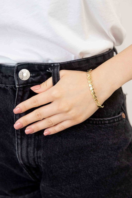 Two Spades cuff bracelets with leaf designs, one in 14k gold plating and one in stainless steel, against a white background.