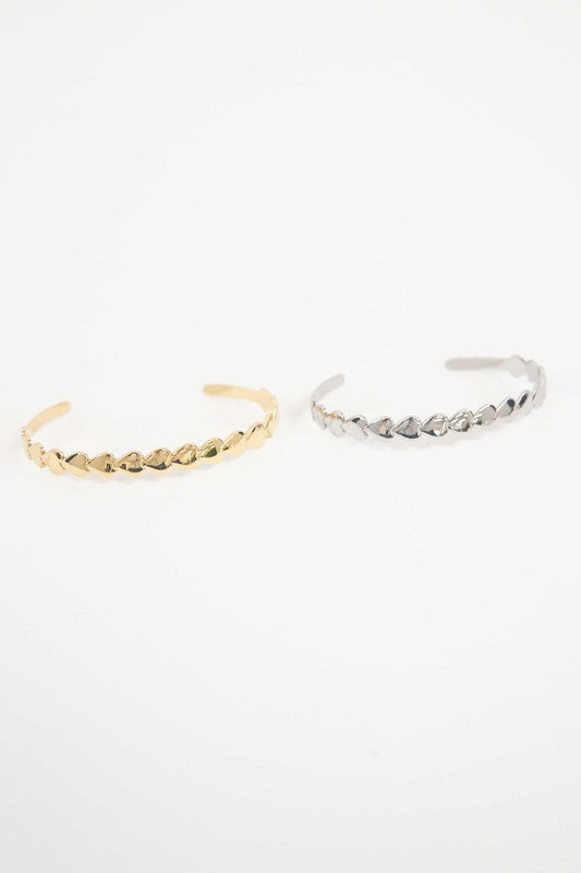 Two Spades cuff bracelets with leaf designs, one in 14k gold plating and one in stainless steel, against a white background.