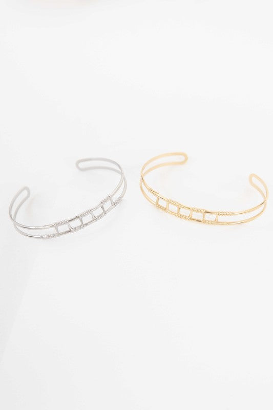 Two Wired Cuff Bracelets, one silver-toned stainless steel and one gold-plated, with gemstone embellishments, displayed against a white background.