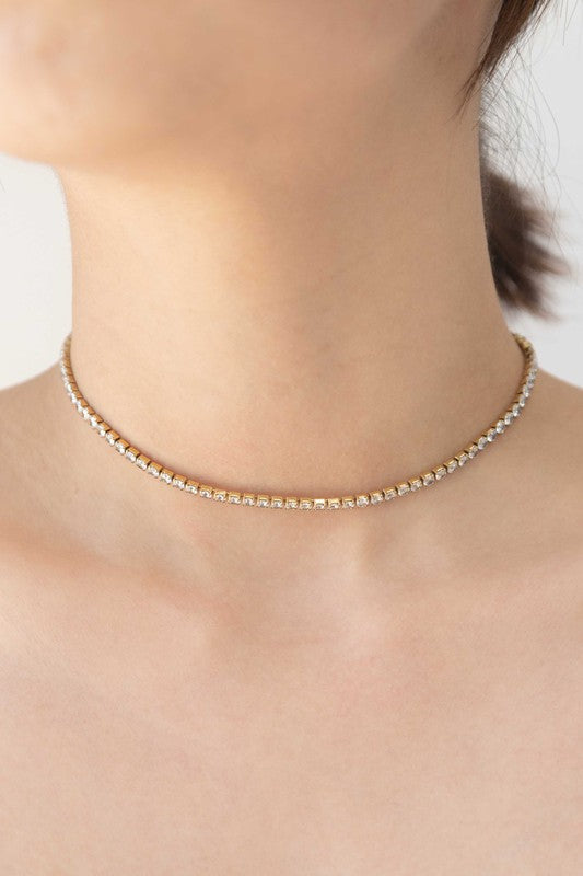Gold-tone round stone tennis necklace with white crystal stones on a silver background.