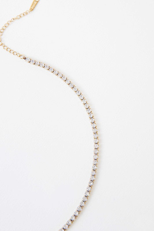 Gold-tone round stone tennis necklace with white crystal stones on a silver background.