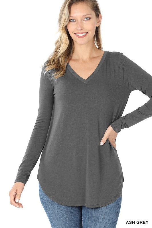 A woman in a relaxed fit, ash grey Long Sleeve V-Neck Round Hem Top and blue jeans poses with her hand on her hip.