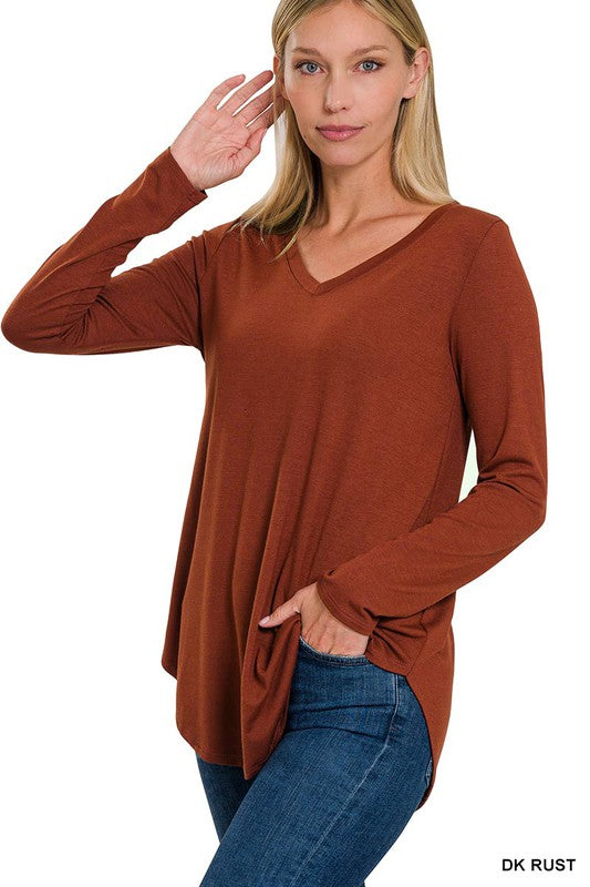 A woman in a relaxed fit, ash grey Long Sleeve V-Neck Round Hem Top and blue jeans poses with her hand on her hip.