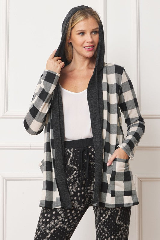 A woman poses indoors wearing the Buffalo Plaid Hooded Cardigan over a white top and patterned black pants. She is smiling and facing slightly to the left. The stylish ensemble, crafted from cozy polyester and spandex, combines comfort with modern flair.