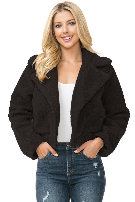 A person is wearing a Women's Faux Fur Jacket in light brown, textured fabric over a white top and blue jeans. They're smiling with their hands in their jacket pockets, exuding an effortlessly chic vibe with the casual solid print of the outfit.