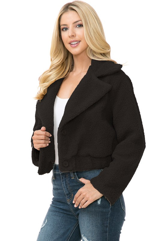 A person is wearing a Women's Faux Fur Jacket in light brown, textured fabric over a white top and blue jeans. They're smiling with their hands in their jacket pockets, exuding an effortlessly chic vibe with the casual solid print of the outfit.