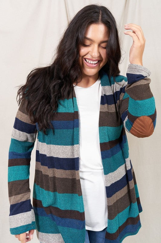 A person stands smiling, dressed in a bestselling multicolored Stripe Elbow Patch Cardigan, paired with a white shirt, blue ripped jeans, and beige sandals against a plain backdrop.