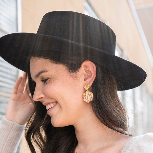 A woman wearing a black wide-brimmed hat, beige sweater, and Roxy Earrings - Pumpkin Spice smiles while looking to the side.