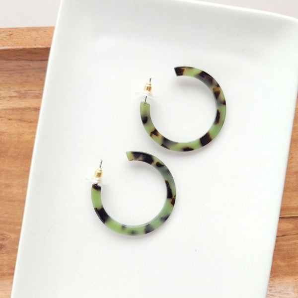 A pair of Camy Earrings in Olive Tortoise, medium-sized with a green and black tortoiseshell pattern, crafted from lightweight acrylics, displayed on a white dish.