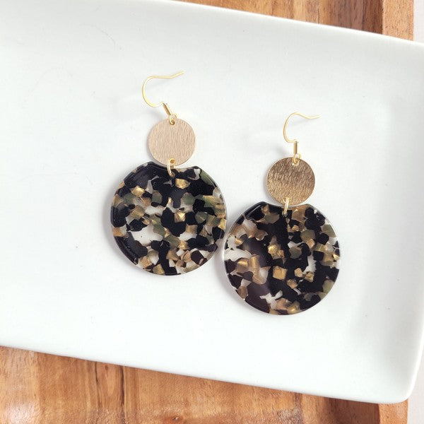A pair of statement Zoey Earrings - Black & Bronze, featuring gold-colored hooks and round resin pendants with a black, brown, and white marbled pattern, crafted from plant-based acetate acrylic and hypoallergenic stainless steel, displayed on a white surface.