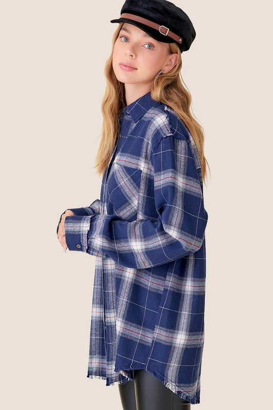 A person with long blonde hair wearing a black cap and an oversized Celine Shirt, which features a blue checkered plaid flannel design, showing a slight smile against a neutral background.