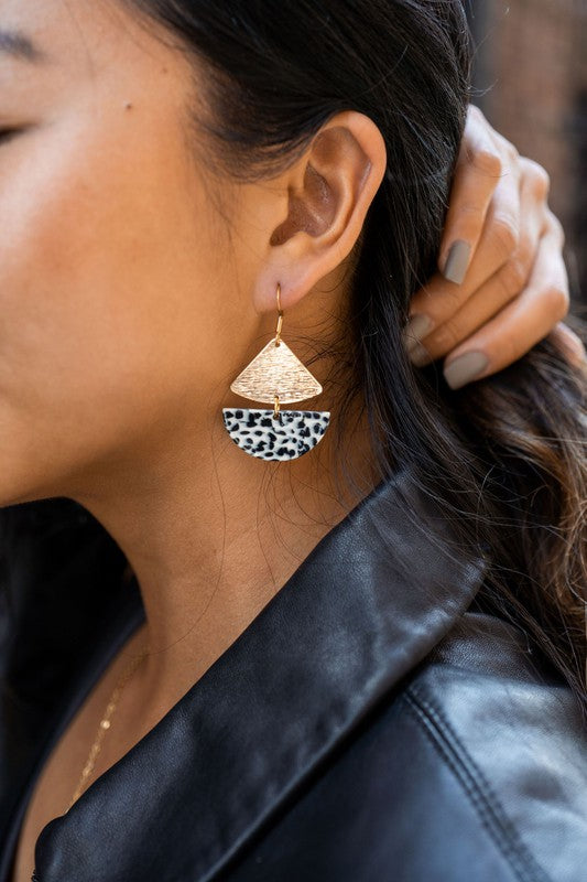 Close-up of a person wearing the Ava Black Dot earrings, featuring gold-plated hooks and a distinctive leopard print. Their dark hair partially obscures their ear while their hand, adorned with neutral-colored nail polish, rests behind their neck.