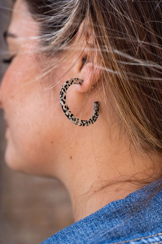 The Camy Hoops - Black Dot are medium-sized hoop earrings featuring a black and white spotted pattern, crafted from lightweight acrylics, elegantly displayed on a white rectangular dish placed on a wooden surface.
