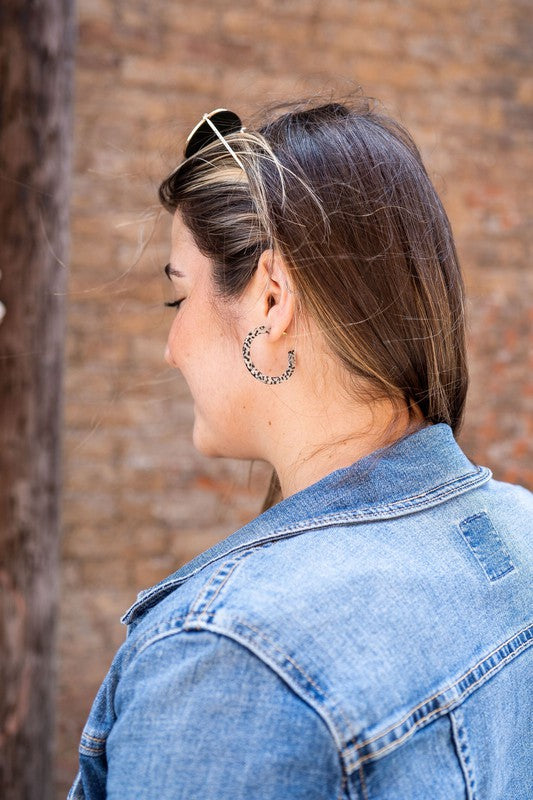 The Camy Hoops - Black Dot are medium-sized hoop earrings featuring a black and white spotted pattern, crafted from lightweight acrylics, elegantly displayed on a white rectangular dish placed on a wooden surface.