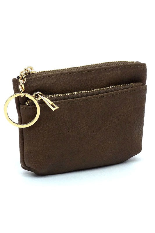 The Fashion Keychain Coin Purse is a compact, textured brown coin holder made from vegan leather. It features a zippered closure, an external pocket, and comes with an attached gold keyring.