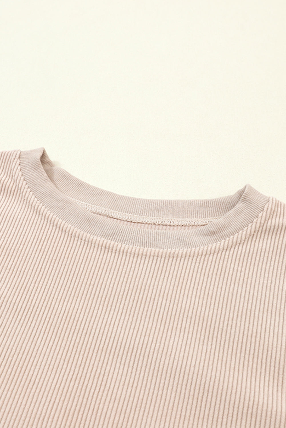 A woman stands outdoors, looking down while touching her hair with one hand. She is wearing an Apricot Ribbed Corduroy Oversized Sweatshirt and white pants, exuding an effortlessly chic and fashionable look.