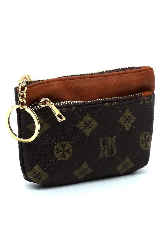 The CM Monogram Keychain Coin Purse is a small, white faux vegan leather pouch adorned with a brown geometric pattern. It features a brown zipper and comes with a gold CM Monogram keychain, along with the letters "CMWD".