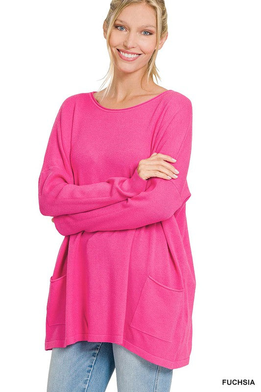 A woman wearing an Oversized Front Pocket Sweater in a cozy, bright pink color smiles while crossing her arms. She also wears light blue jeans.