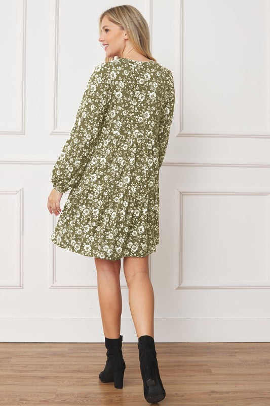 A person wearing a green Floral Crew Neck Midi Dress and black ankle boots smiles while walking inside against a white backdrop.