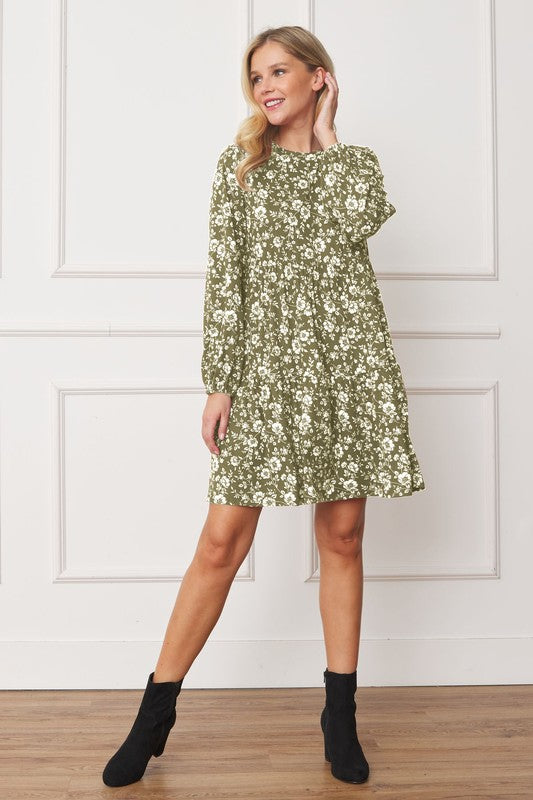 A person wearing a green Floral Crew Neck Midi Dress and black ankle boots smiles while walking inside against a white backdrop.