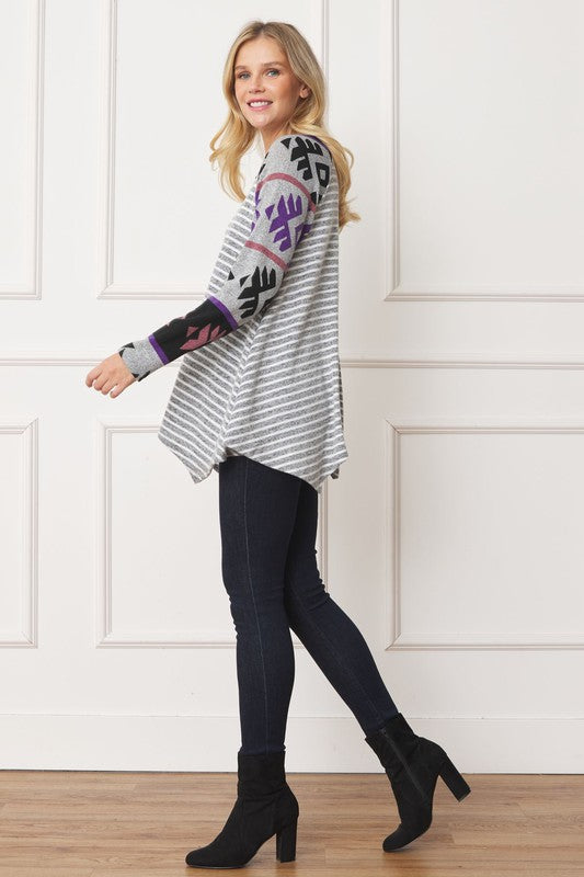 Woman wearing a Tribal Sleeve Handkerchief Tunic, featuring long sleeves with a geometric pattern, made from Polyester Spandex Fabric, standing against a white wall.