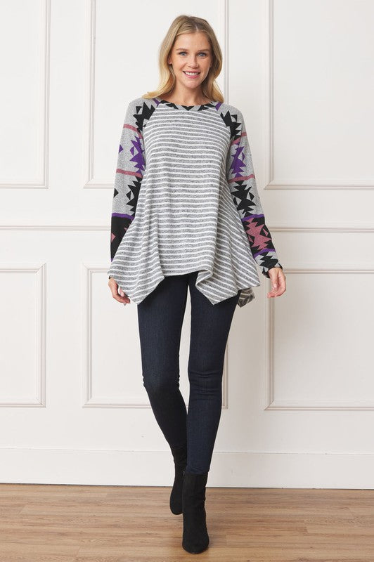 Woman wearing a Tribal Sleeve Handkerchief Tunic, featuring long sleeves with a geometric pattern, made from Polyester Spandex Fabric, standing against a white wall.