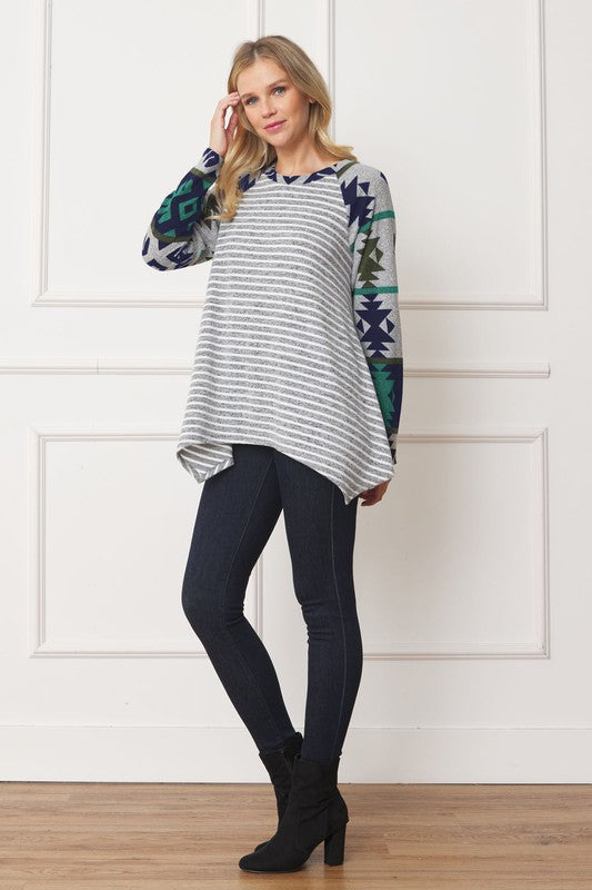 Woman wearing a Tribal Sleeve Handkerchief Tunic, featuring long sleeves with a geometric pattern, made from Polyester Spandex Fabric, standing against a white wall.