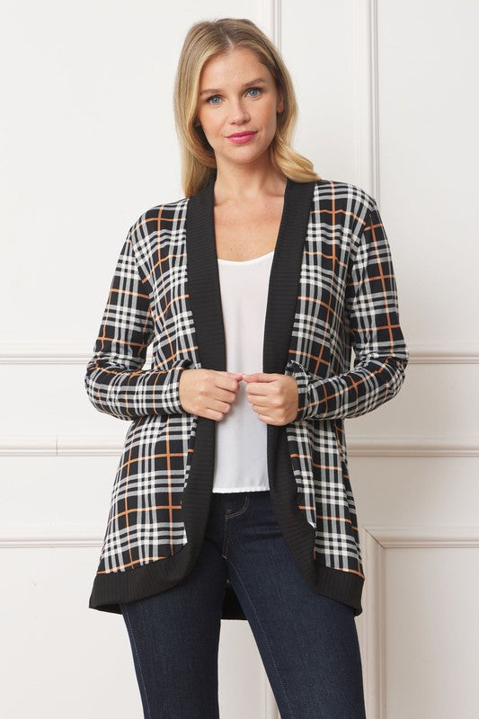 A woman with blonde hair stands against a white background, looking at the camera with a neutral expression. She is wearing the Plaid Contrast Drape Open Cardigan over a white top and dark jeans. Made in the United States, this cardigan features a stylish black and white plaid design.