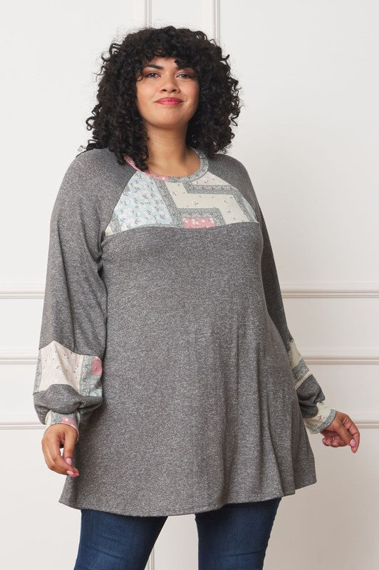 A person with curly hair is wearing a long-sleeved brown Plus Patchwork Panel Accent A-Line Tunic, standing in front of a white wall.