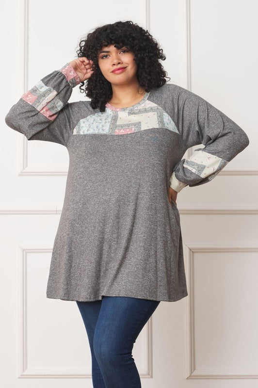A person with curly hair is wearing a long-sleeved brown Plus Patchwork Panel Accent A-Line Tunic, standing in front of a white wall.