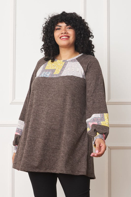 A person with curly hair is wearing a long-sleeved brown Plus Patchwork Panel Accent A-Line Tunic, standing in front of a white wall.