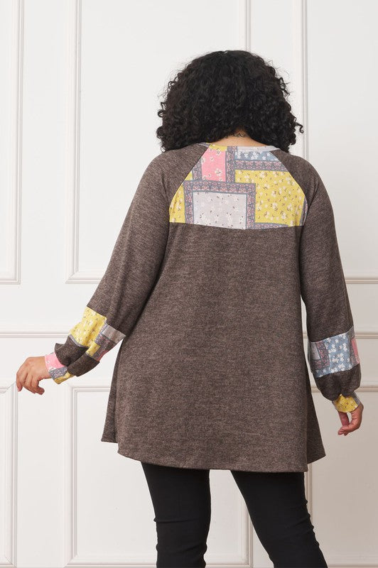 A person with curly hair is wearing a long-sleeved brown Plus Patchwork Panel Accent A-Line Tunic, standing in front of a white wall.
