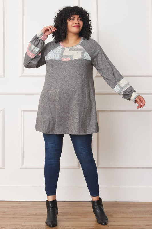 A person with curly hair is wearing a long-sleeved brown Plus Patchwork Panel Accent A-Line Tunic, standing in front of a white wall.