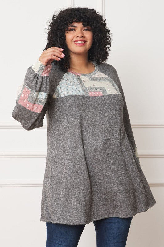 A person with curly hair is wearing a long-sleeved brown Plus Patchwork Panel Accent A-Line Tunic, standing in front of a white wall.