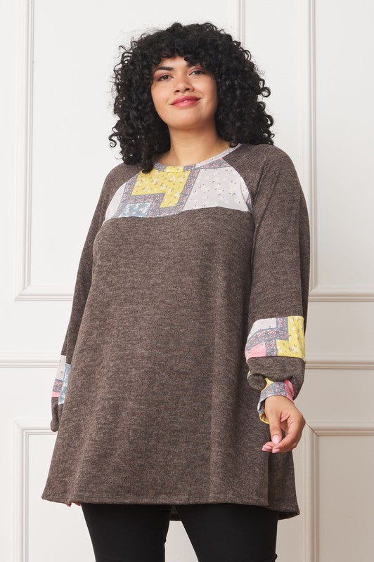 A person with curly hair is wearing a long-sleeved brown Plus Patchwork Panel Accent A-Line Tunic, standing in front of a white wall.
