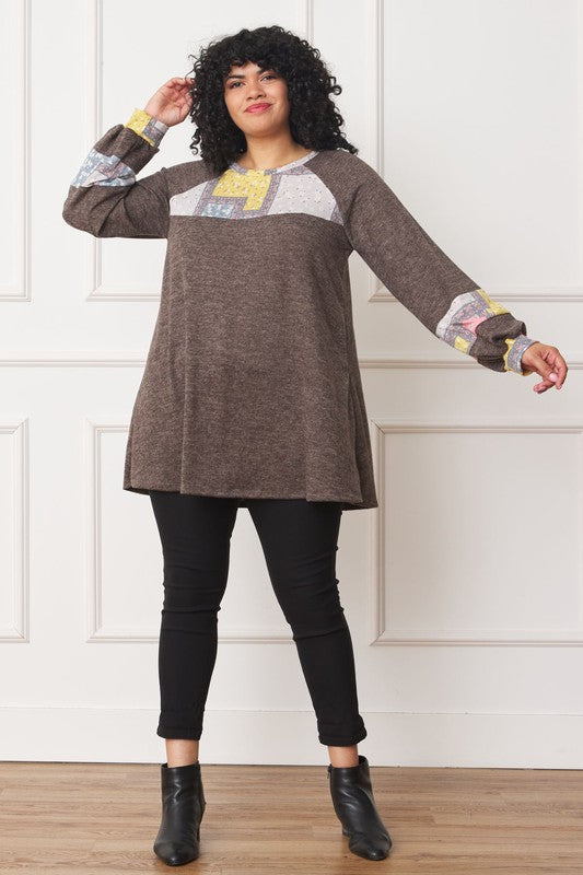 A person with curly hair is wearing a long-sleeved brown Plus Patchwork Panel Accent A-Line Tunic, standing in front of a white wall.