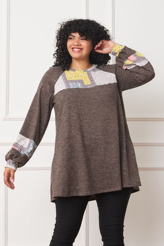 A person with curly hair is wearing a long-sleeved brown Plus Patchwork Panel Accent A-Line Tunic, standing in front of a white wall.