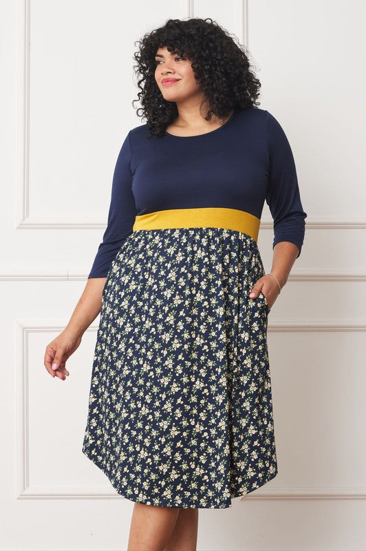 A woman with curly hair smiles, adorning a Plus Curved Hem Band Midi Dress made from a polyester and spandex blend. The black dress showcases three-quarter sleeves and is accented with a red waistband. The skirt is decorated with an eye-catching floral pattern of large pink and orange flowers.